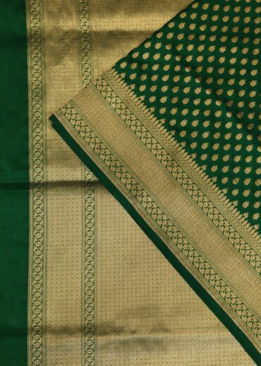 Banarasi silk saree in bottle green colour with all over small zari butis and zari border. Comes with a running blouse.